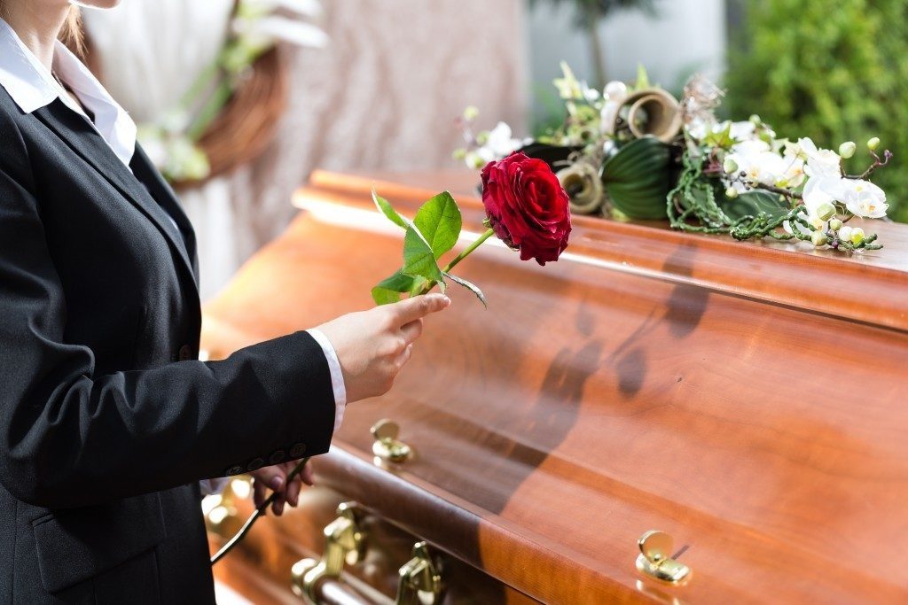 Woman holding a red rose beside the casket