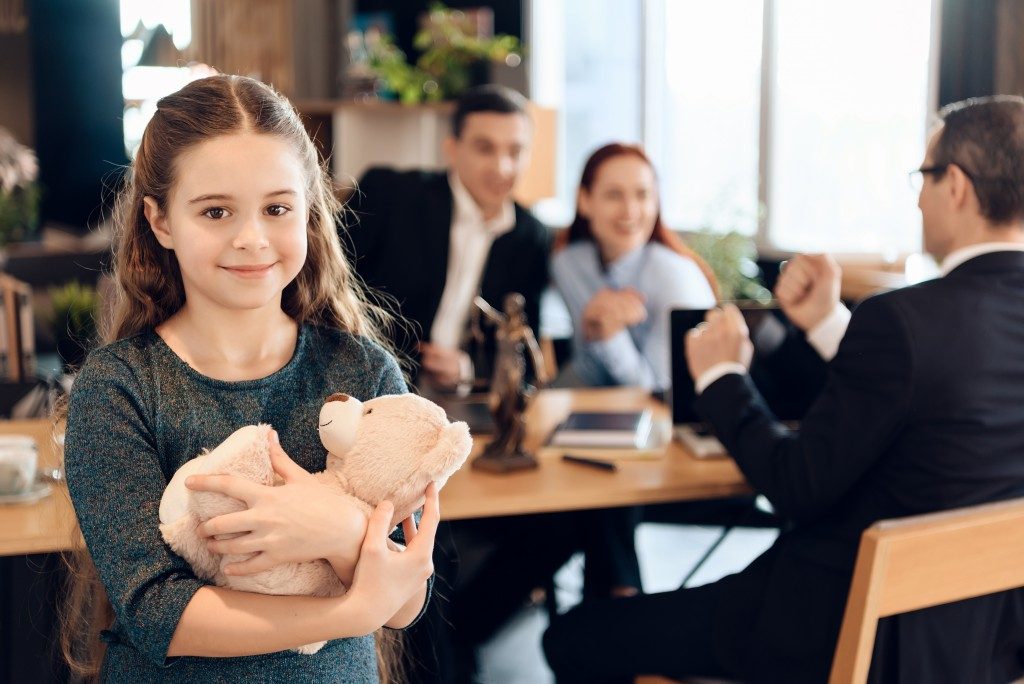 little girl holding a teddy bear with her parents and a lawyer at the back