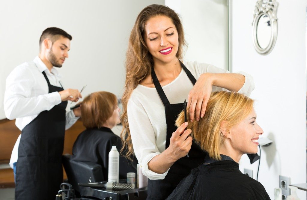 Smiling client sitting in a hair salon while hairdresser is combing her hair