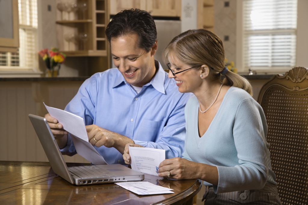 A couple happily paying bills online with a laptop computer in their house