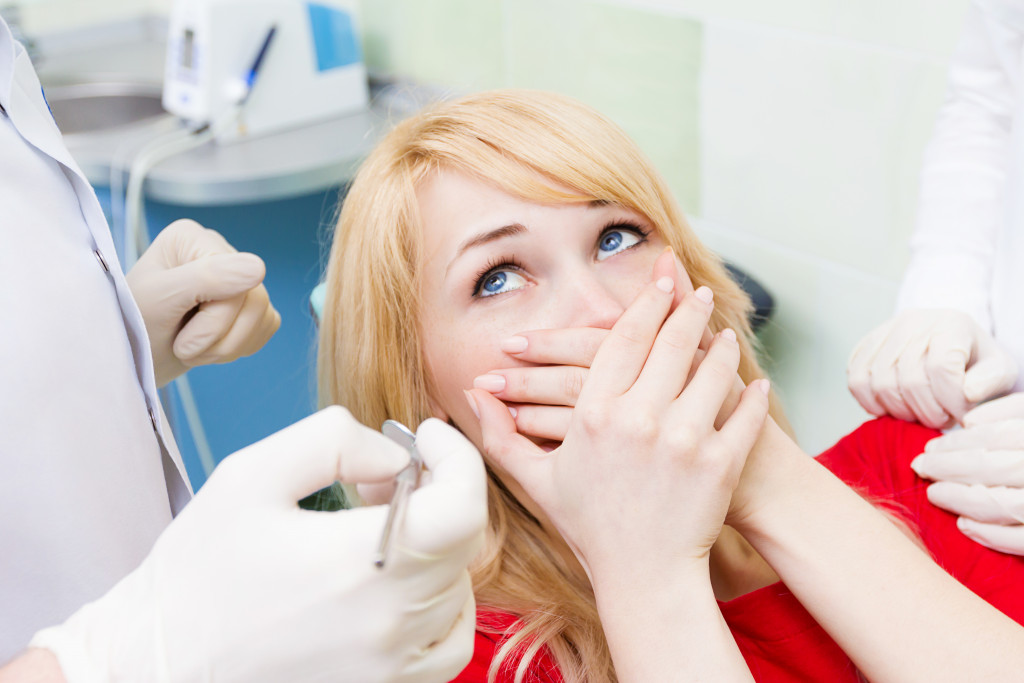 a woman covers her mouth as the dentist stands in front of her