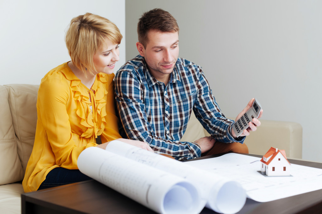 Couple talks about home improvement plans with blueprints and mini toy house in front of them