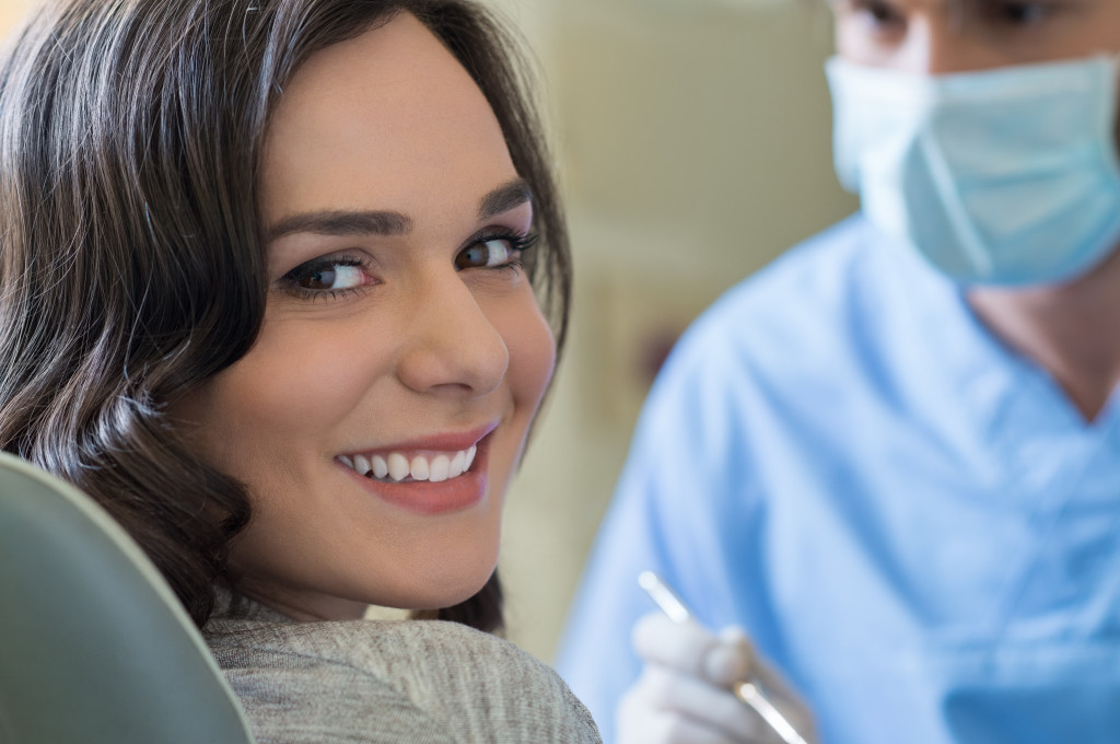 A woman smiling at the camera while a dentist gets in position in front of her