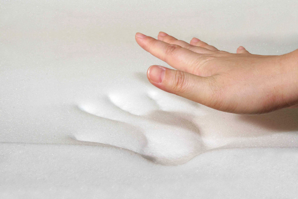 A hand touching a memory foam mattress