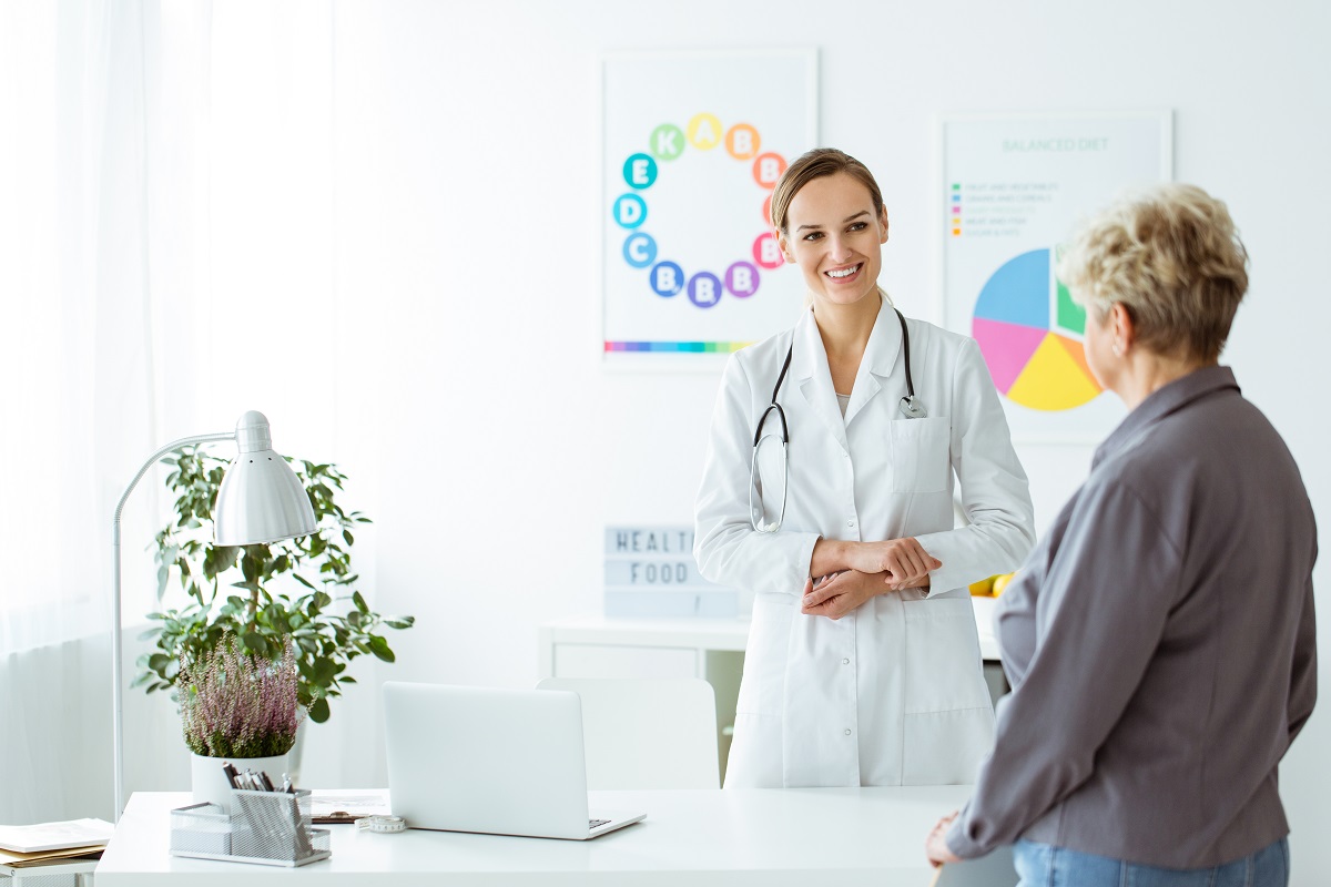 female doctor smiling at elderly patient entering her white clinic