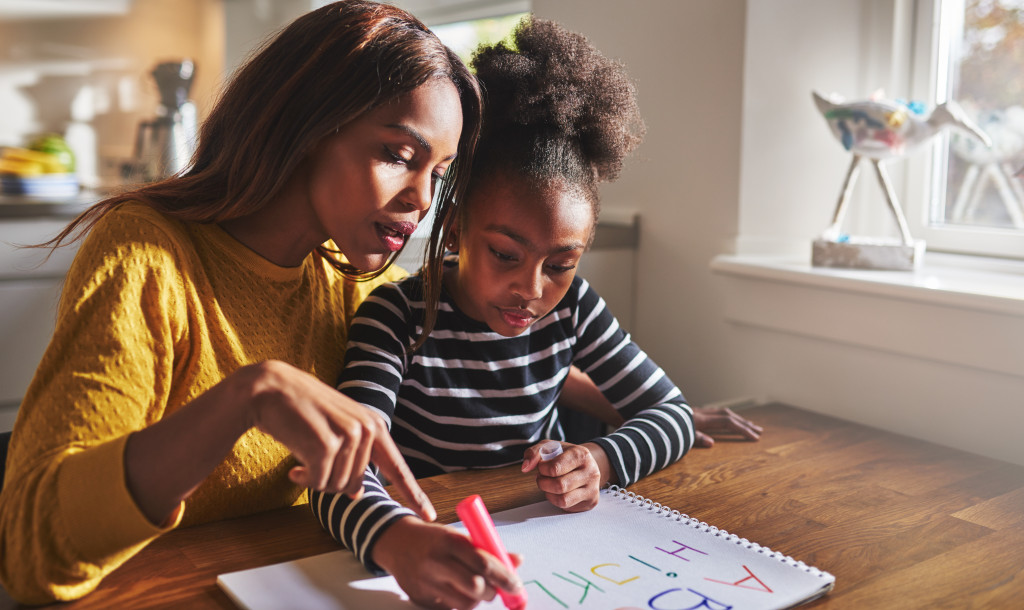 Mother helping her daughter to read the alphabet at home.